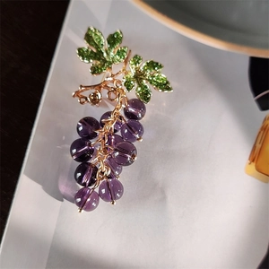 Detail of grape brooch with purple beads and green enamel leaves on golden base