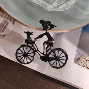 Broche silhouette noire représentant une fille à vélo avec un chiot dans le panier