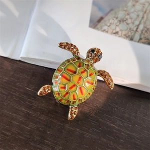 Detailed view of turtle brooch with green enamel shell and amber rhinestones on gold base