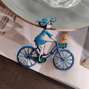 Détail d'une broche en émail montrant une fille à vélo avec un chien sur fond bleu