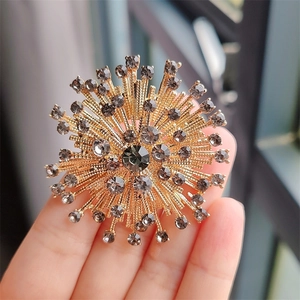 Close-up of a vintage sunburst brooch with golden base and gray rhinestones