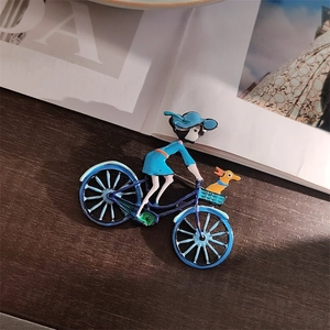 Détail d'une broche en émail représentant une fille à vélo avec un chien en bleu
