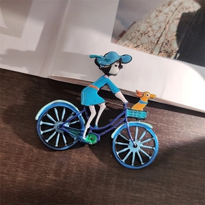 Détail d'une broche en émail montrant une fille à vélo avec un petit chien dans le panier