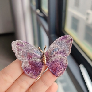 Macro detail of purple embroidered butterfly brooch with fine gold metallic body