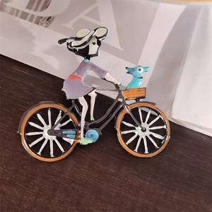 Broche en émail montrant une fille à vélo avec un chien bleu sur fond en bois