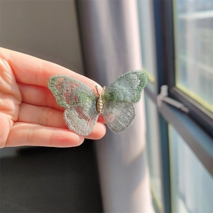 Detail of embroidered green lace butterfly brooch with golden metal body in hand