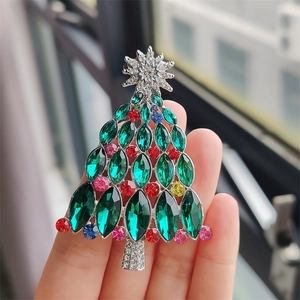 Gros plan d'une broche sapin de Noël argentée avec cristaux verts tenue à la main