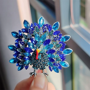 Detailed view of a vintage turkey brooch with blue rhinestones held in hand for size