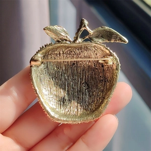 Detail view of the brushed gold apple brooch showing the secure pin back clasp mechanism
