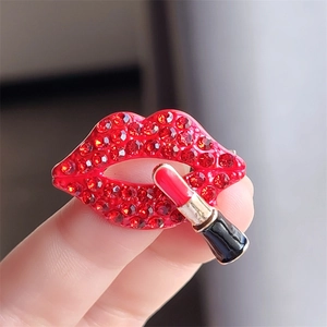 Detailed close-up of crystal lips and lipstick brooch held between fingers for scale
