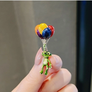 Detail of colorful frog balloon enamel pin held by hand to show compact mini size