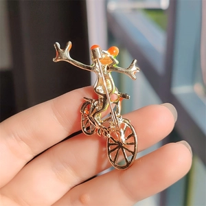 Macro shot of creative frog riding bicycle brooch in gold metal with orange enamel finish