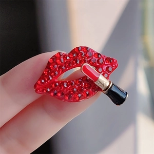 Close-up of a sparkling red crystal lip brooch with a mini gold lipstick charm pendant
