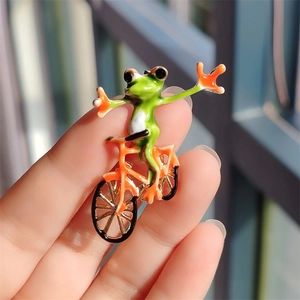 Detail of creative green frog cycling enamel brooch held in hand with glossy finish