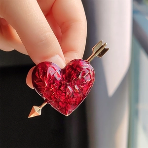 Detail of red enamel heart and gold arrow brooch held to show actual size and texture
