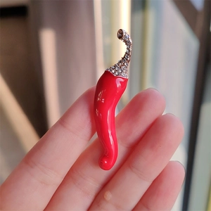Broche piment rouge étincelante avec cristaux et émail tenue dans une main