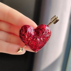 Exquisite Cupid heart brooch with red enamel and golden arrow on a hand background