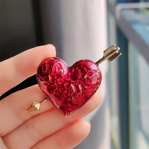 Close-up of heart-shaped brooch with red crinkled foil texture and golden arrow detail