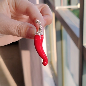 Vue à la main d'une broche piment en émail rouge avec des strass en cristal étincelants