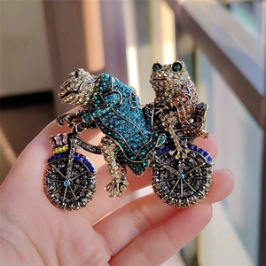 Detailed macro view of vintage frog riding bicycle brooch with colorful crystals