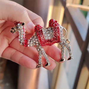 Close-up of golden camel brooch featuring red and clear rhinestones on a metal base