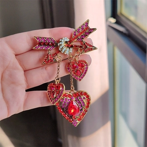 Détail de la broche flèche de Cupidon avec strass rubis et glands dorés tenue à la main