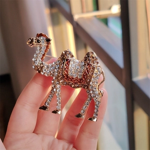Macro shot of hand holding vintage camel brooch with clear crystals and brown enamel details