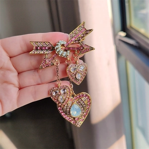 Détail de la broche flèche de Cupidon dorée avec strass roses et pendentif cœur opale