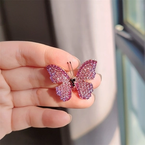 Handheld view of a delicate pink and purple gradient rhinestone butterfly brooch