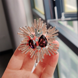 Macro detail of luxury crystal sunburst brooch with purple teardrop gemstones in hand