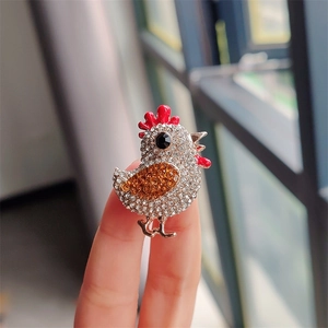 Broche coq argentée tenue en main avec cristaux et détails en émail rouge
