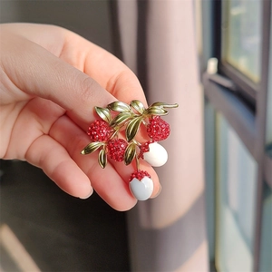 Detailed view of handmade lychee brooch with red crystals and white glaze on green leaves