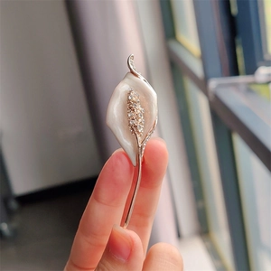 Macro detail of calla lily brooch with white enamel petals and sparkling rhinestones