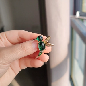 Macro detail of hummingbird brooch with emerald green gemstones and gold crystal wings
