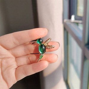 Elegant gold hummingbird brooch with emerald green gemstones and sparkling crystals