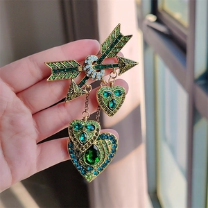 Vue détaillée d'une broche vintage dorée avec cristaux verts et pendentifs cœurs