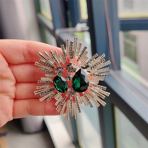 Close-up of vintage crystal brooch with deep green gemstones and silver sunburst rays