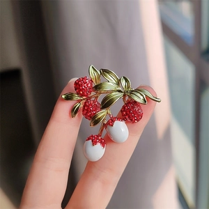 Close-up of a lychee fruit brooch featuring red crystals and green enamel leaves