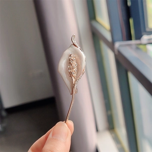 Detailed close-up of a white calla lily brooch with gold plating and sparkling crystals