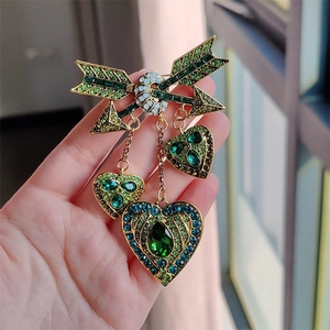 Détail de la broche cœur flèche dorée avec cristaux verts et bleus et pendentifs pompons