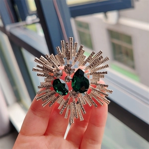 Detail of vintage sunburst brooch with green gemstones and white crystals in light gold