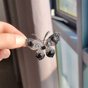 Detailopname van een vlinderbroche met fonkelende steentjes en zwarte kralen in de hand