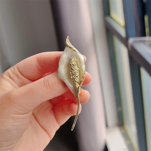 Detailed macro view of gold Calla Lily brooch with white enamel and sparkling crystals