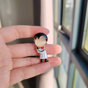 Détail d'une broche docteur cartoon avec pierre œil de chat tenue entre les doigts