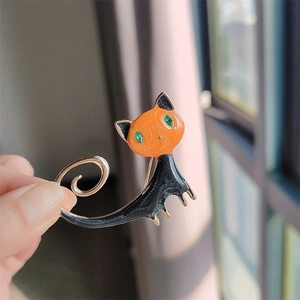 Detail einer niedlichen orange-schwarzen Emaille-Katzenbrosche in der Hand, die die Größe zeigt