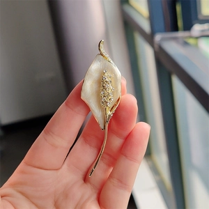 Macro detail of calla lily brooch with white enamel petals and sparkling crystal stamens