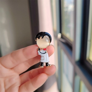 Détail d'une broche docteur cartoon en métal doré avec une pierre œil-de-chat
