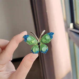 Detailopname van een gouden vlinderbroche met groene en blauwe strass steentjes