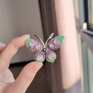 Detail van gouden vlinderbroche met paarse strass steentjes en roze opaalstenen