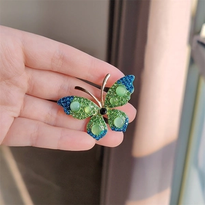 Gedetailleerde close-up van een vlinderbroche met groene strass en kattenoogstenen